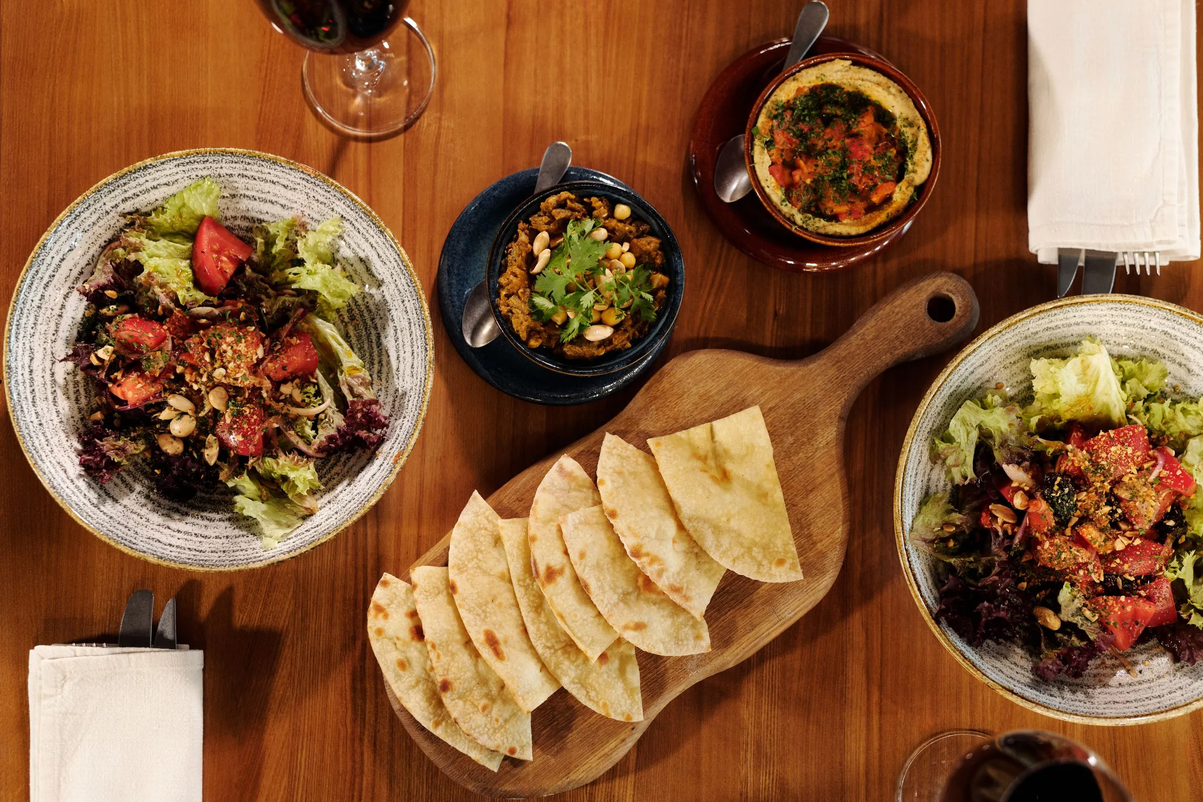 Salads, warm bread and a clay dish on a wooden board.